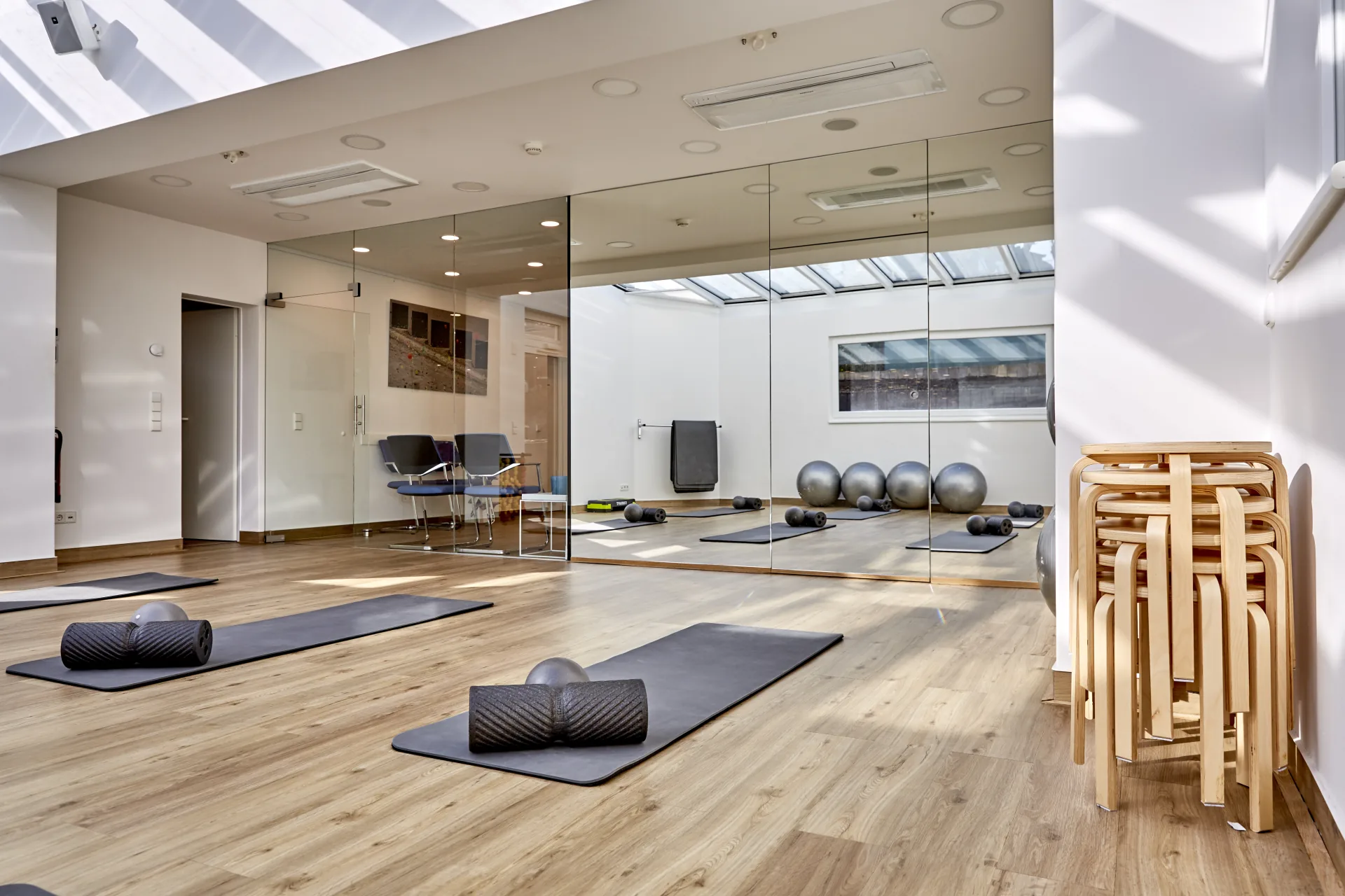 Ein lichtdurchfluteter, moderner Gymnastikraum mit ausgelegten Trainingsmatten, Faszienrollen und einer großen Spiegelwand in der Praxis PHYSIOMED SÜD Berlin für aktive Physiotherapie-Stellenangebote.