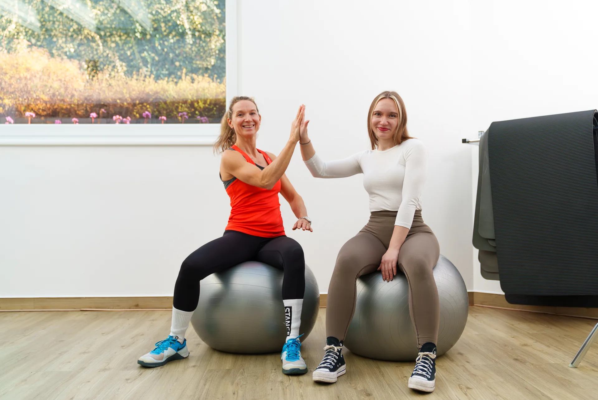 Motivierte Mitarbeiterinnen lächeln beim High-Five auf Pezzibällen im Kursraum von PHYSIOMED SÜD Berlin – werde Teil unseres Teams für Physiotherapie in Berlin.